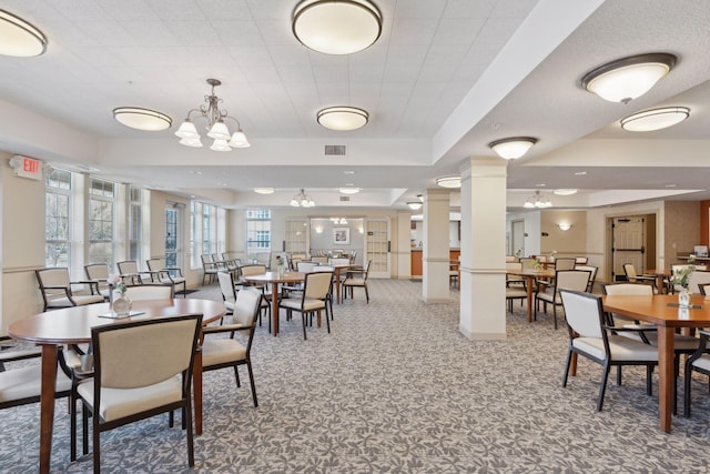 dining area with a raised ceiling, carpet flooring, a chandelier, and decorative columns