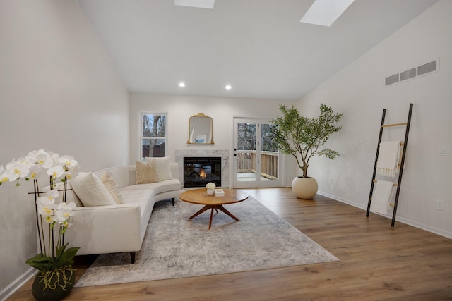 living room with wood-type flooring, vaulted ceiling with skylight, and a fireplace