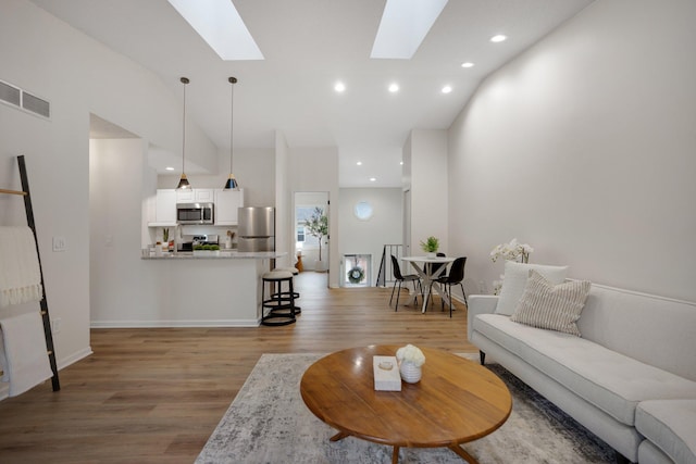 living room with a high ceiling, light wood-type flooring, and a skylight