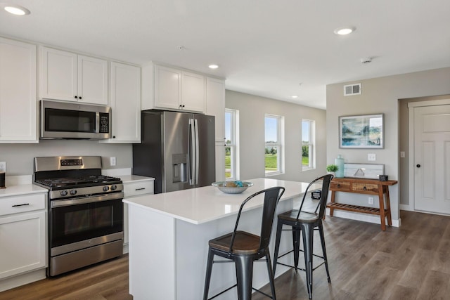 kitchen with white cabinetry, a kitchen bar, a center island, stainless steel appliances, and dark wood-type flooring