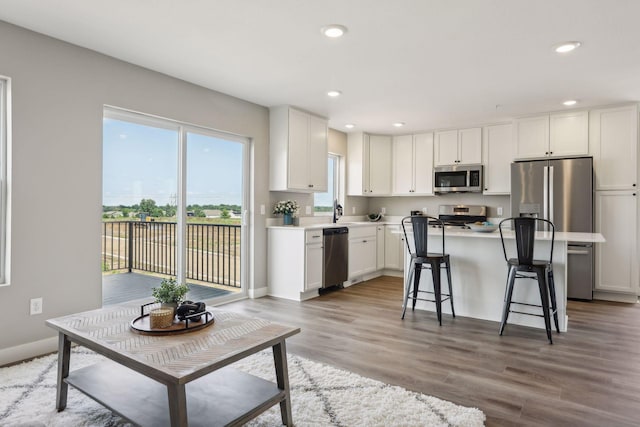 kitchen with white cabinetry, wood-type flooring, a kitchen breakfast bar, a center island, and stainless steel appliances