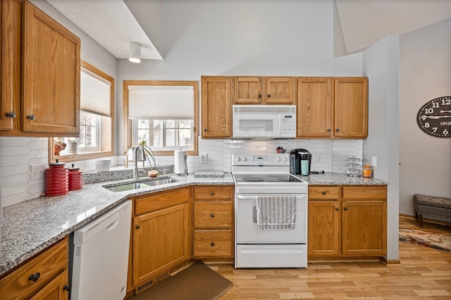 kitchen with light wood-type flooring, white appliances, a sink, and light stone countertops