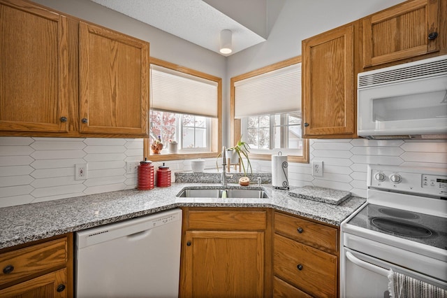 kitchen featuring white appliances, backsplash, a sink, and light stone counters