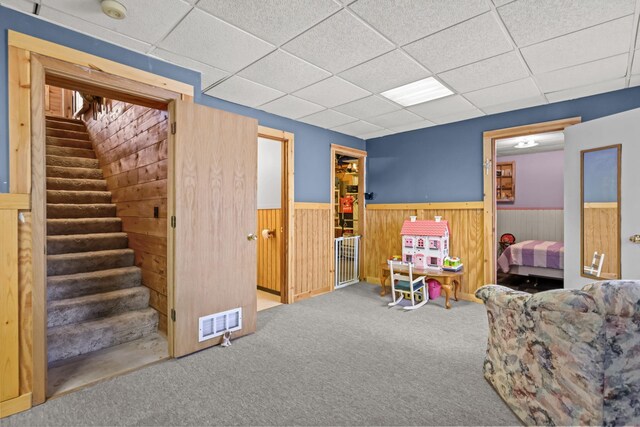 recreation room with wood walls, carpet flooring, and a drop ceiling