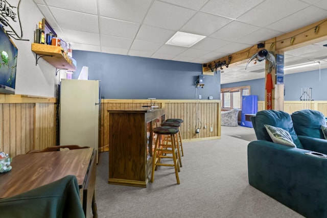 bar featuring light colored carpet, a paneled ceiling, white fridge, and wood walls