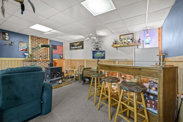 bar featuring carpet flooring, a paneled ceiling, a wood stove, and wood walls