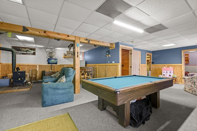 recreation room with a wood stove, a drop ceiling, wooden walls, and carpet flooring