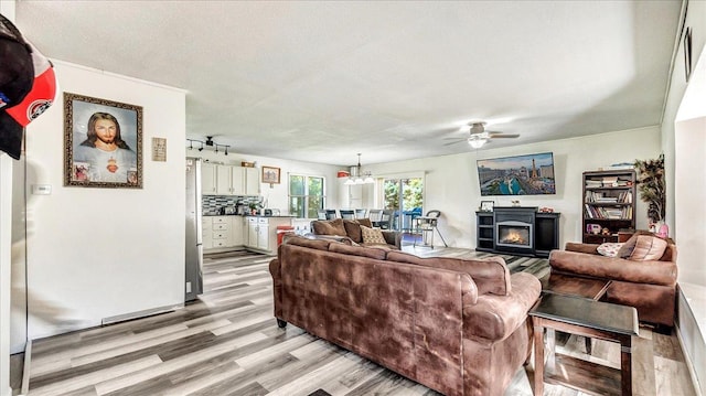 living room with ceiling fan with notable chandelier, light hardwood / wood-style flooring, and a textured ceiling