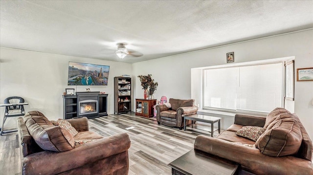 living room featuring ceiling fan, light hardwood / wood-style flooring, and a textured ceiling