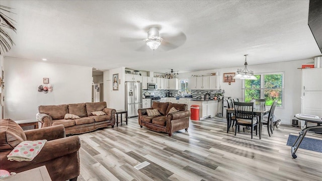 living room featuring ceiling fan, a textured ceiling, and light wood-type flooring