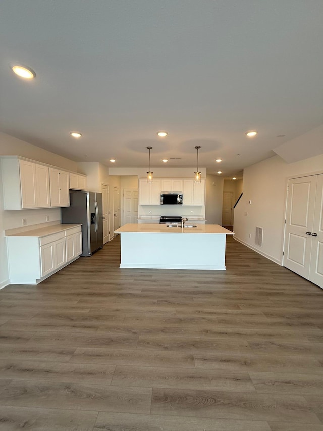 kitchen featuring hardwood / wood-style floors, decorative light fixtures, white cabinetry, an island with sink, and stainless steel appliances