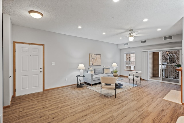 living room with ceiling fan, a textured ceiling, and light wood-type flooring