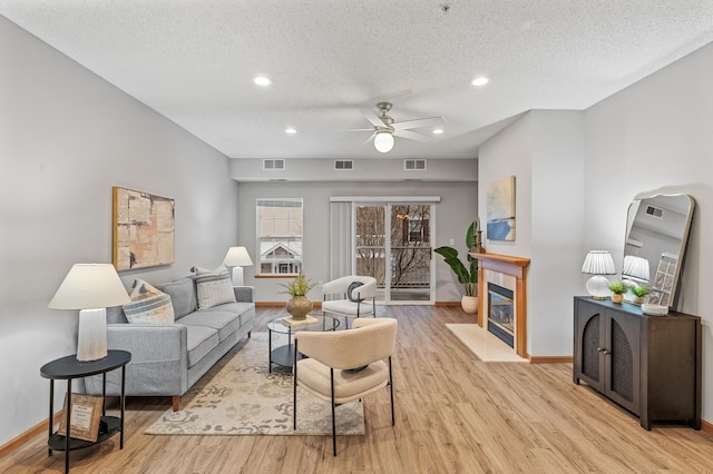 living room featuring ceiling fan, light hardwood / wood-style floors, a tile fireplace, and a textured ceiling