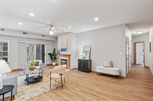 living room featuring ceiling fan, a fireplace, light hardwood / wood-style floors, and a textured ceiling