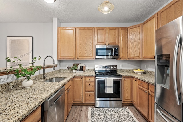 kitchen featuring sink, light hardwood / wood-style flooring, stainless steel appliances, light stone countertops, and a textured ceiling