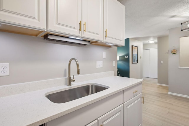 kitchen featuring light stone counters, light hardwood / wood-style floors, sink, and white cabinets