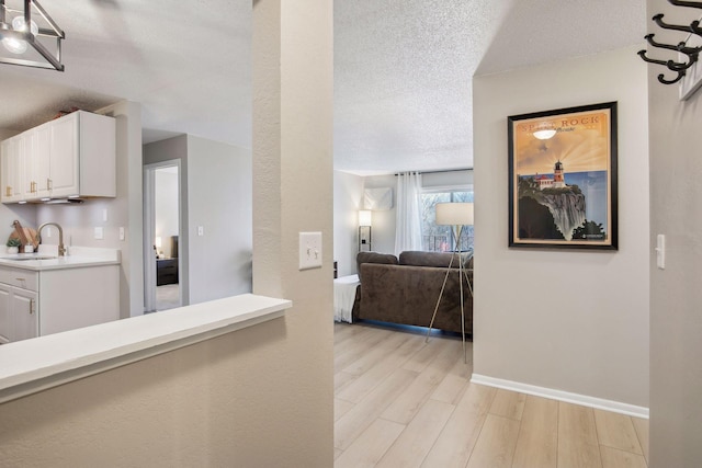 hallway with sink, a textured ceiling, and light wood-type flooring