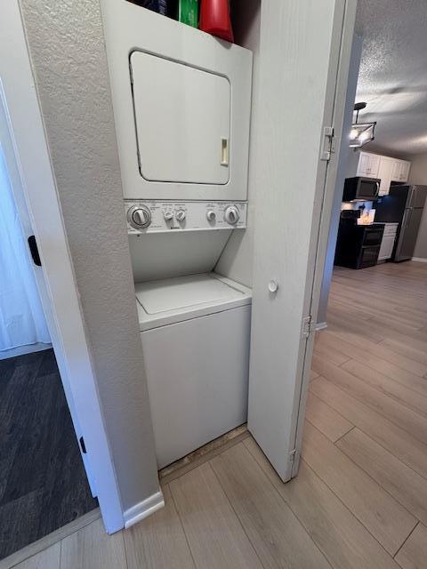 washroom with stacked washer / drying machine, light hardwood / wood-style floors, and a textured ceiling