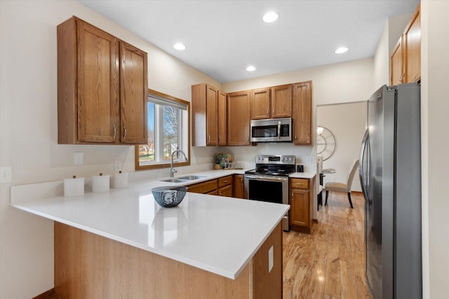 kitchen with sink, light wood-type flooring, kitchen peninsula, and appliances with stainless steel finishes