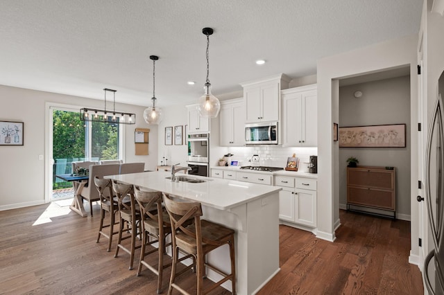 kitchen featuring a breakfast bar area, appliances with stainless steel finishes, white cabinetry, hanging light fixtures, and a center island with sink