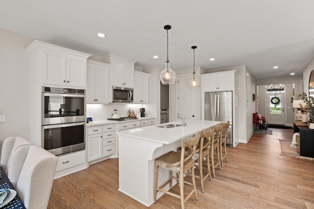 kitchen featuring stainless steel appliances, decorative light fixtures, a center island with sink, and white cabinets