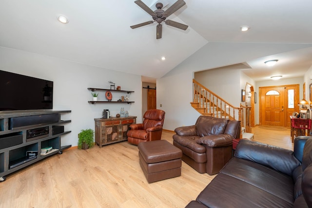 living room with ceiling fan, a barn door, vaulted ceiling, and light hardwood / wood-style flooring