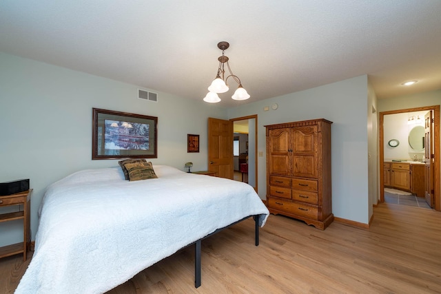 bedroom with ensuite bath, a chandelier, sink, and light hardwood / wood-style flooring