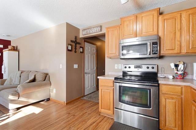 kitchen featuring stainless steel appliances, light brown cabinetry, a textured ceiling, and light wood-type flooring