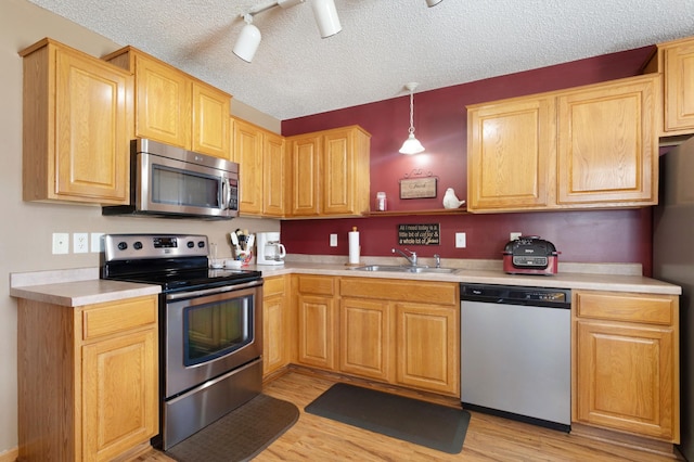 kitchen featuring hanging light fixtures, appliances with stainless steel finishes, sink, and light hardwood / wood-style flooring