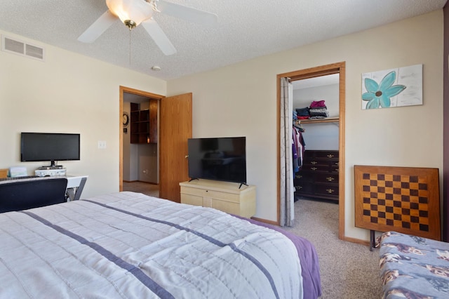 carpeted bedroom with ceiling fan, a walk in closet, a textured ceiling, and a closet