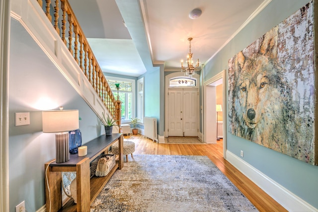 entrance foyer featuring an inviting chandelier, crown molding, radiator heating unit, and light hardwood / wood-style flooring