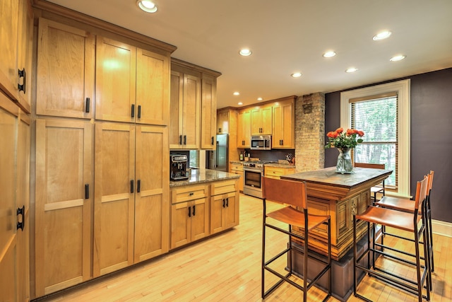 kitchen featuring appliances with stainless steel finishes, a breakfast bar area, dark stone countertops, and light hardwood / wood-style flooring