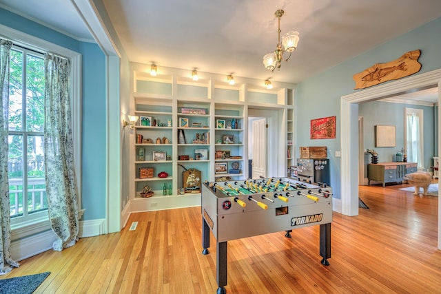 game room with a notable chandelier, plenty of natural light, built in features, and light wood-type flooring