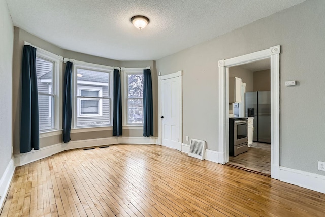 spare room with a textured ceiling and light hardwood / wood-style floors