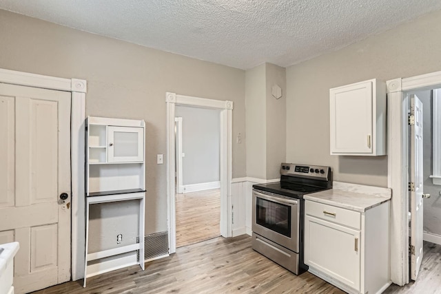 kitchen with electric stove, white cabinetry, light hardwood / wood-style flooring, and a textured ceiling