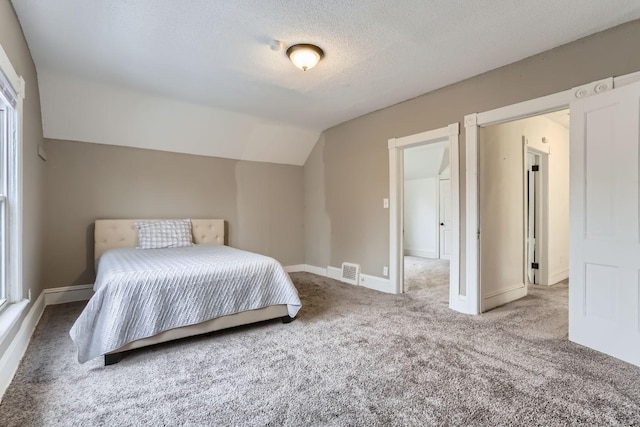 bedroom with vaulted ceiling, carpet flooring, and a textured ceiling