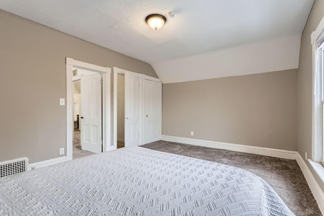 unfurnished bedroom featuring vaulted ceiling, a textured ceiling, and carpet