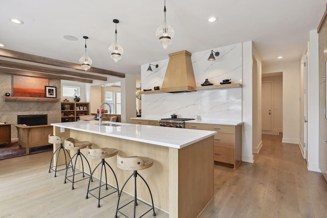 kitchen featuring sink, hanging light fixtures, light hardwood / wood-style flooring, custom range hood, and decorative backsplash