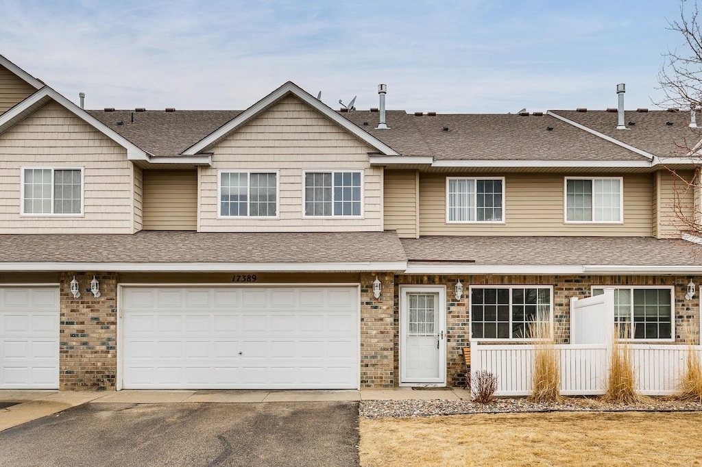 multi unit property featuring a shingled roof, brick siding, driveway, and an attached garage