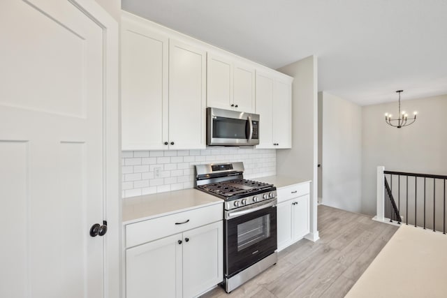 kitchen featuring pendant lighting, appliances with stainless steel finishes, white cabinets, decorative backsplash, and light wood-type flooring