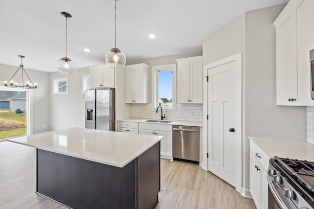 kitchen with a kitchen island, appliances with stainless steel finishes, sink, white cabinets, and hanging light fixtures