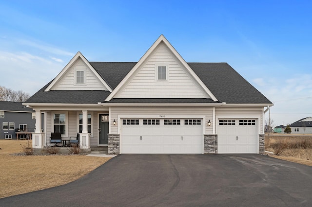 view of front of property featuring driveway, a porch, stone siding, and a shingled roof