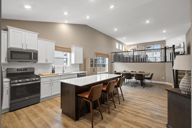 kitchen with appliances with stainless steel finishes, a kitchen island, a sink, and light wood-style floors