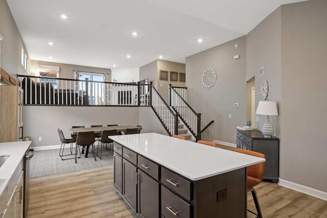 kitchen featuring light wood-style flooring, a breakfast bar area, light countertops, stainless steel dishwasher, and recessed lighting