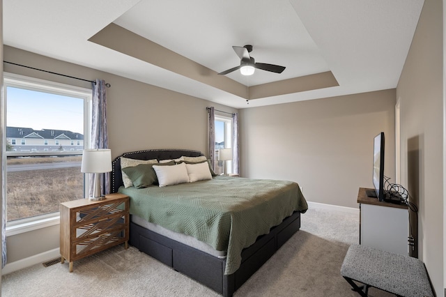 bedroom with light colored carpet, a tray ceiling, visible vents, and baseboards