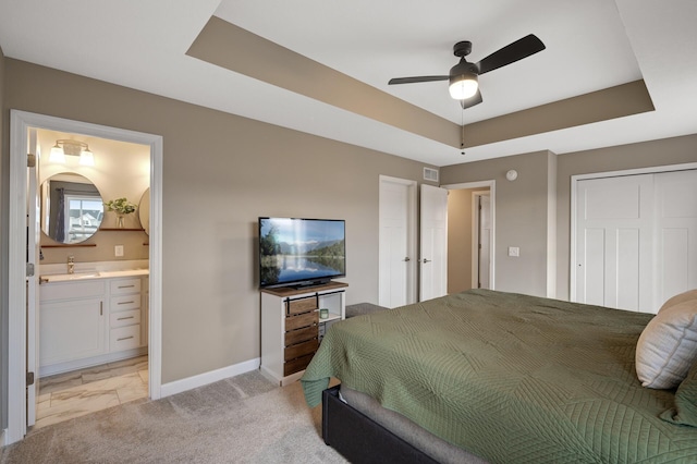 bedroom with ensuite bath, baseboards, a raised ceiling, and light colored carpet