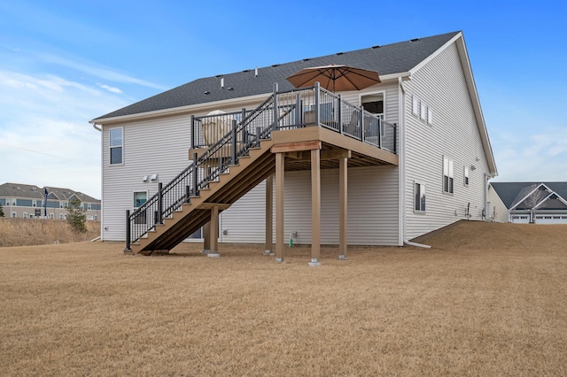 rear view of house with a deck, roof with shingles, a yard, and stairway