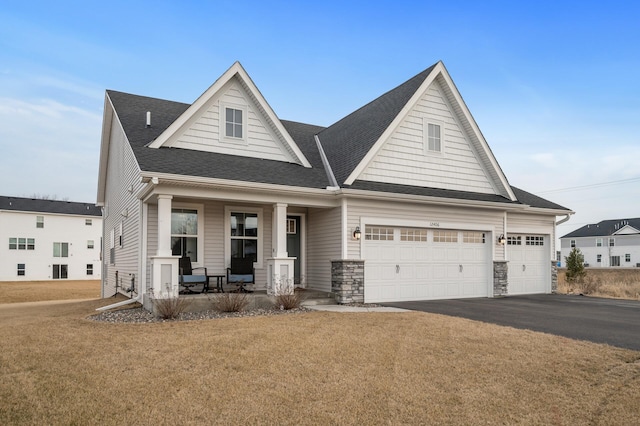 view of front facade with aphalt driveway, a shingled roof, covered porch, an attached garage, and a front yard