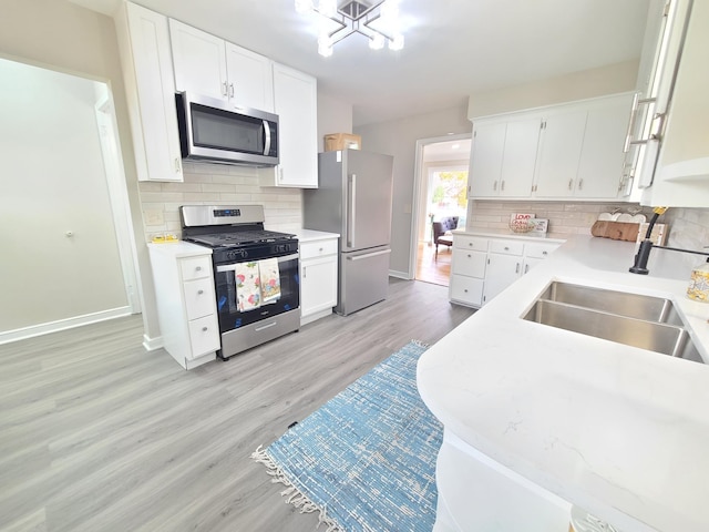 kitchen featuring appliances with stainless steel finishes, tasteful backsplash, sink, white cabinets, and light hardwood / wood-style flooring