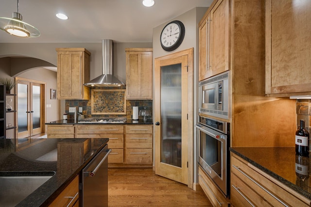 kitchen with tasteful backsplash, hanging light fixtures, light brown cabinets, stainless steel appliances, and wall chimney range hood